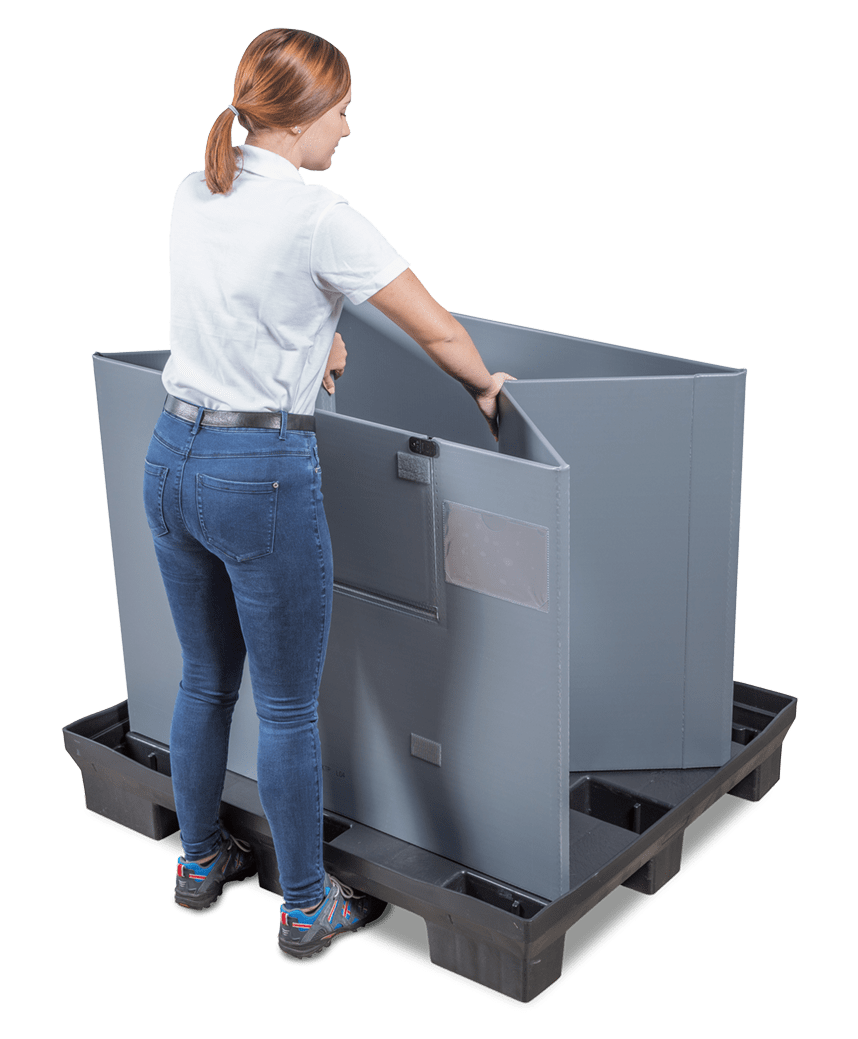 A person in a white shirt and blue jeans is adjusting a large gray fabric container on a black pallet.