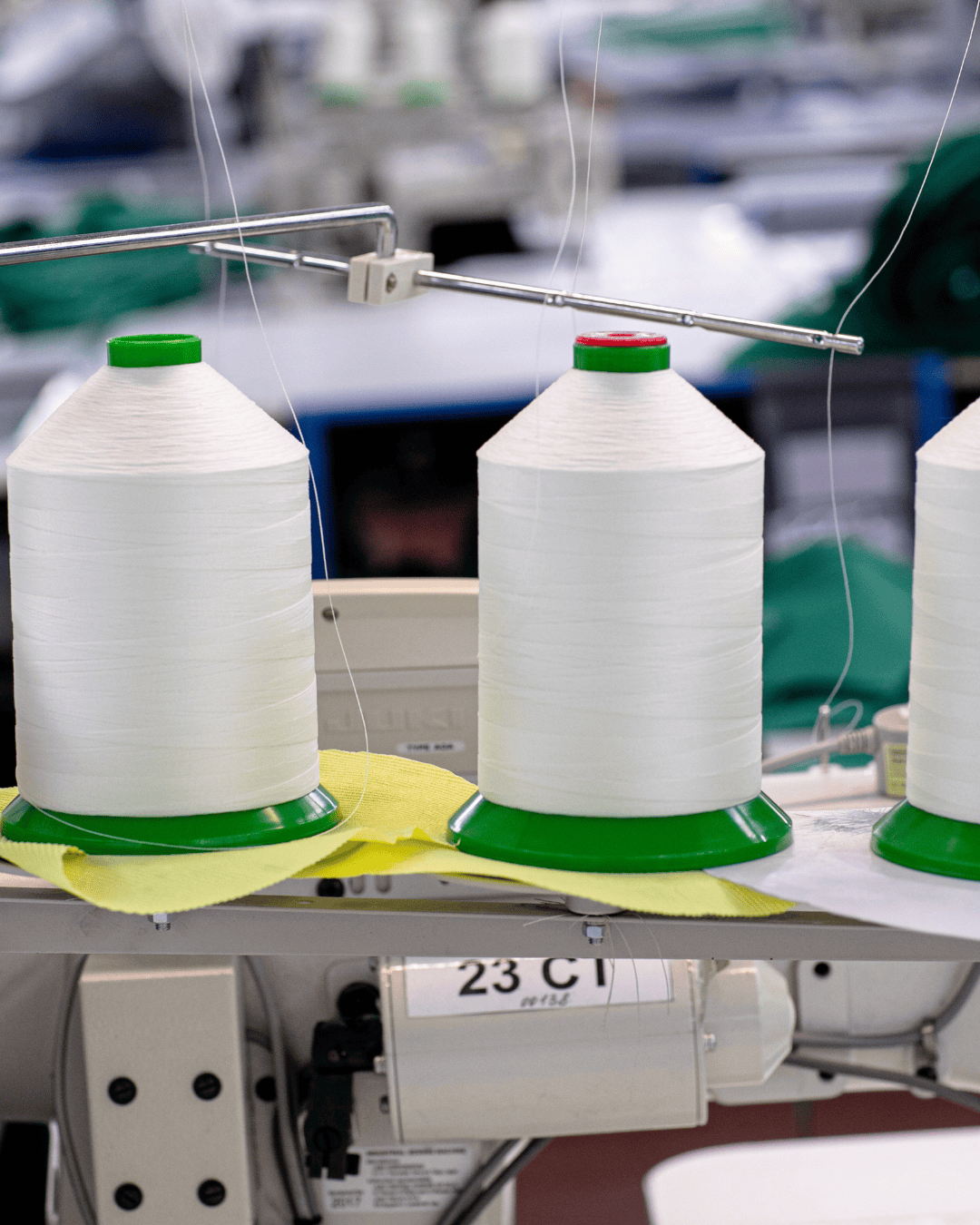 Three spools of white sewing thread with green bases are positioned on a sewing machine, with a yellow fabric piece underneath.