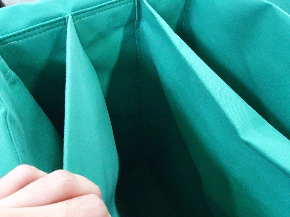 A close-up image of a person's hand holding the edge of an empty teal fabric bag with several internal compartments.