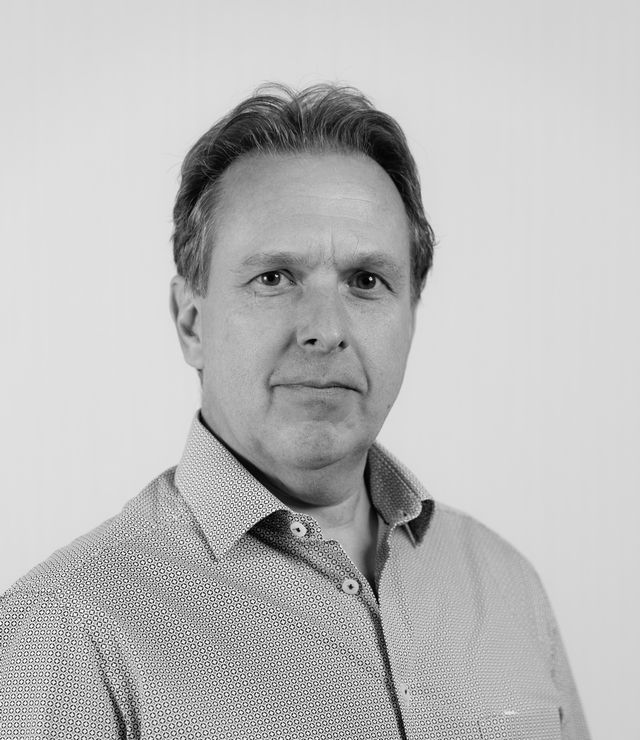 A portrait of a middle-aged man with short hair, wearing a patterned button-up shirt, against a neutral background.