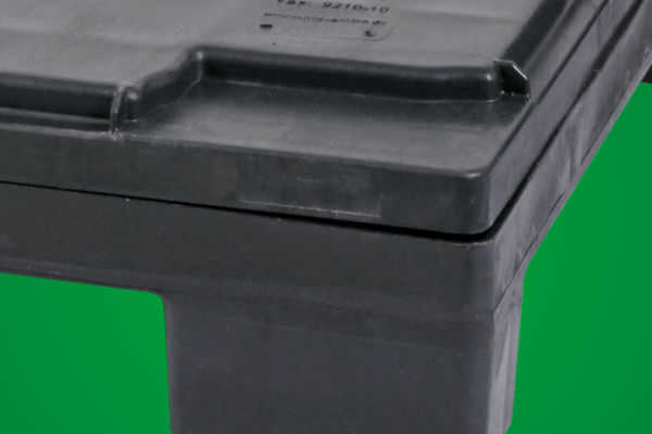 A close-up view of a black plastic container with a flat lid and raised edges, resting on a green background.