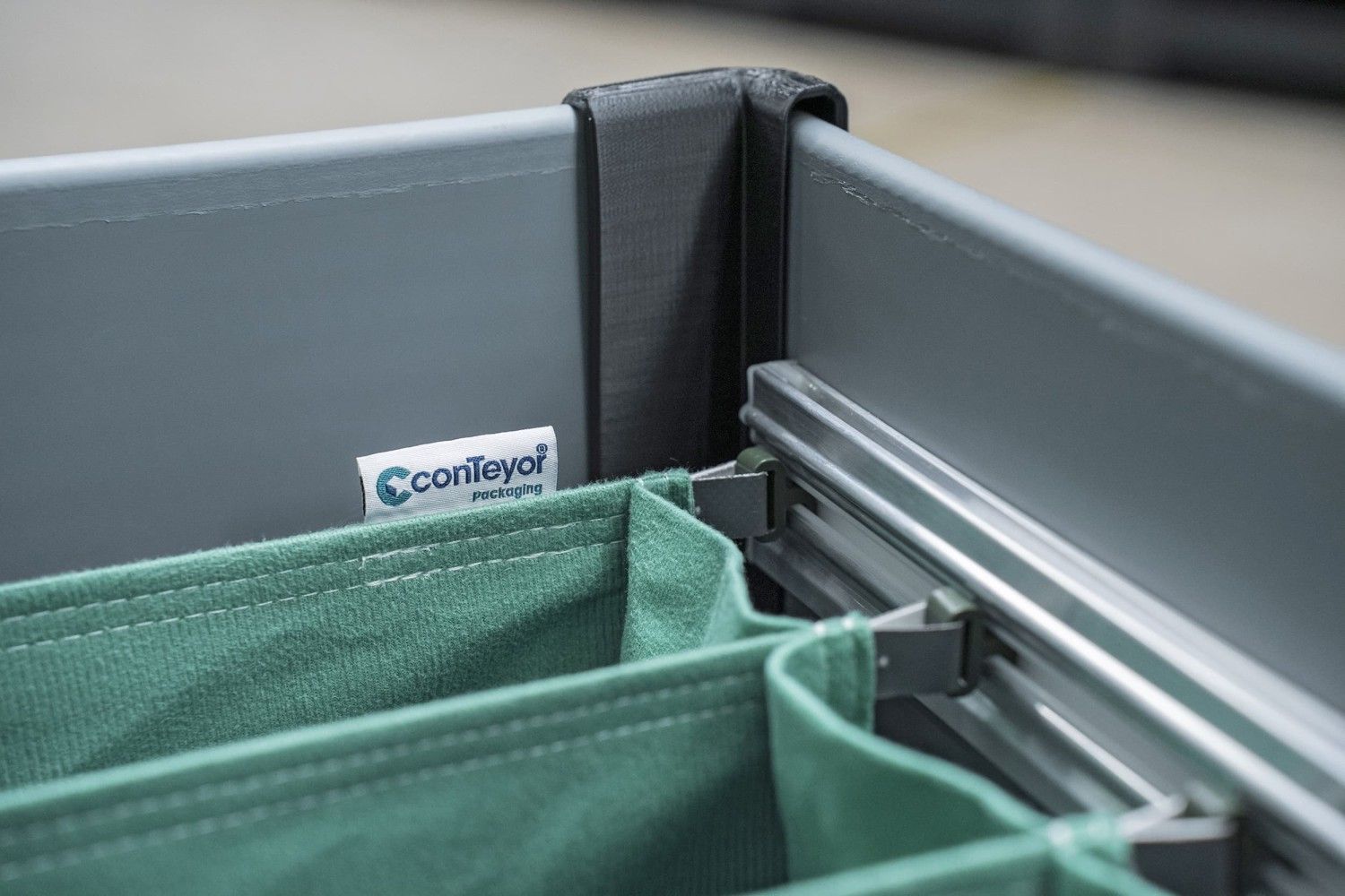 Close-up of a gray storage container with green fabric inserts and a label that reads "conTeyor packaging."