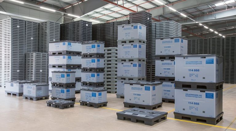 A warehouse filled with stacked crates and pallets, many labeled with "Volkswagen AG," organized for storage and inventory management.