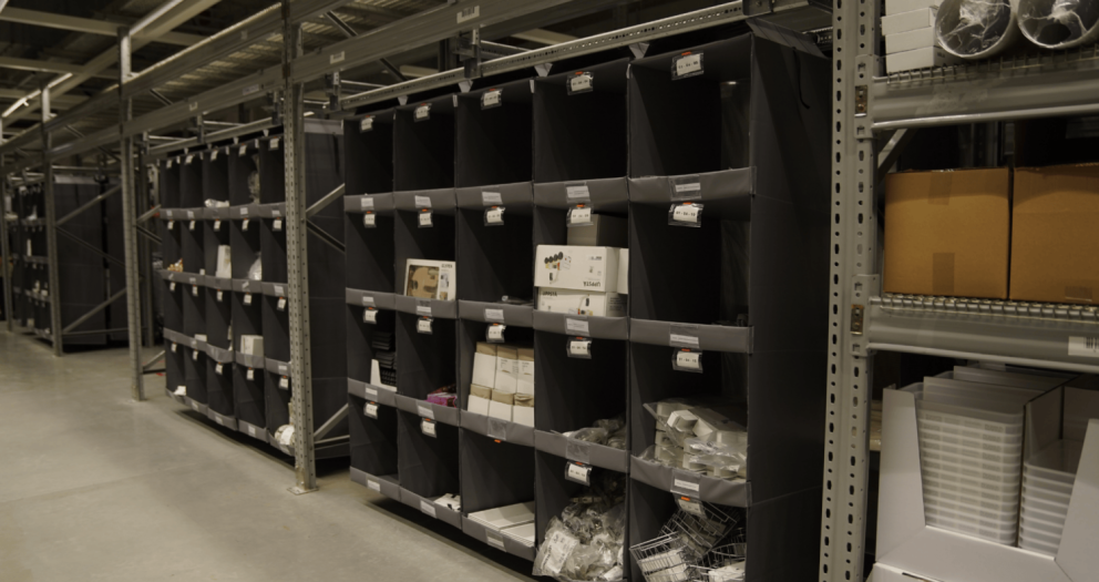 A warehouse aisle with shelving units displaying various products and empty bins.