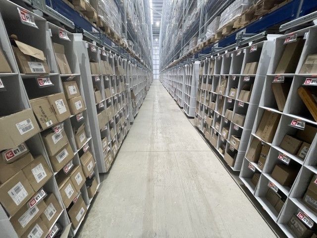 A view of a large storage warehouse aisle with shelves filled with cardboard boxes on both sides.