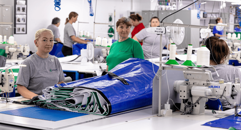 Several workers in a sewing factory are engaged in craft, with a focus on a blue tarp being prepared at the forefront.