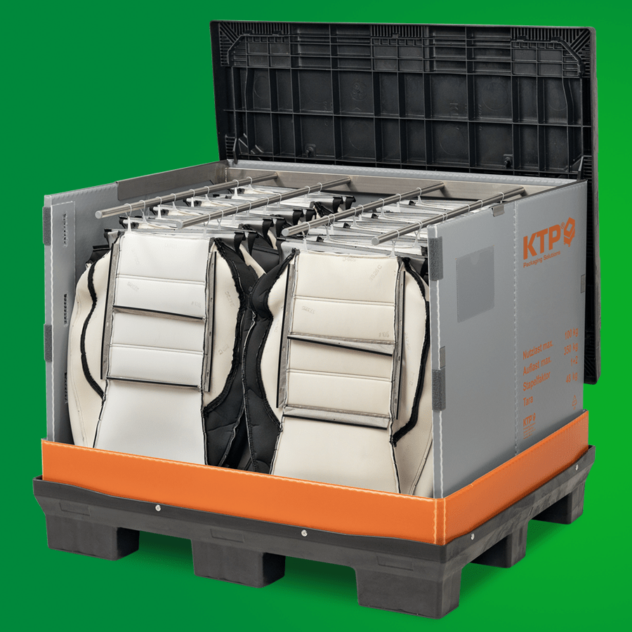 A gray and orange container on a black pallet holding white and black packing bags, with the lid open and labeled "KTP" on the side, against a green background.