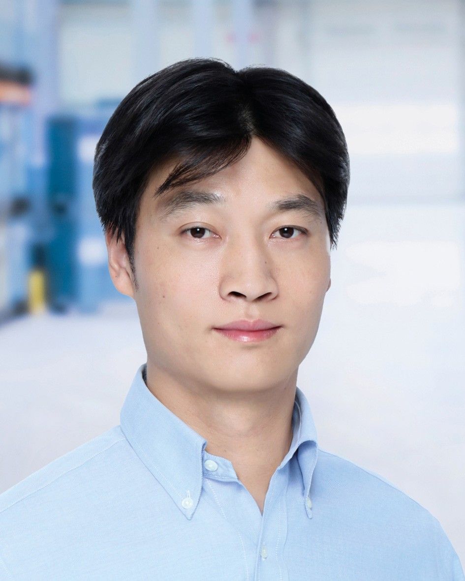 A portrait of a young man with dark hair wearing a light blue shirt, set against a blurred background.