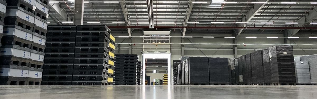 Warehouse interior with stacked pallets of varying colors and heights, and an open entrance in the background.