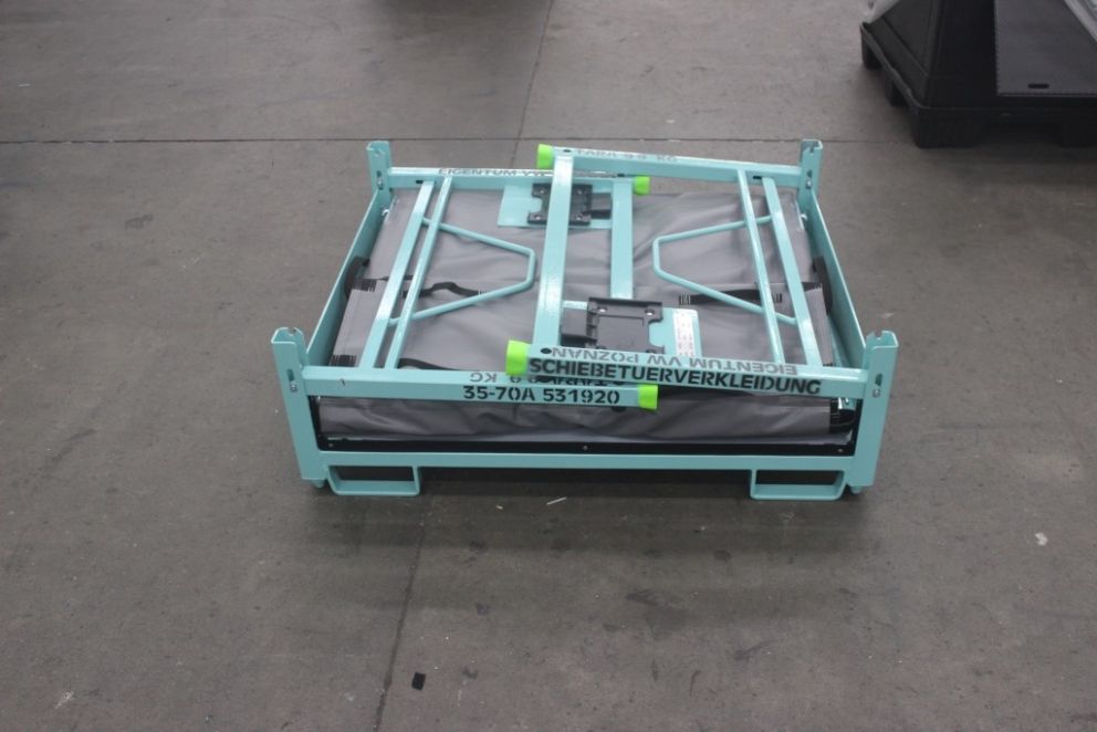 A folded bed frame with a turquoise metal frame and gray fabric, lying on a warehouse floor.