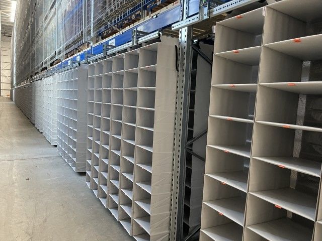 A row of empty, white shelving units in a warehouse, with a clear aisle in between.