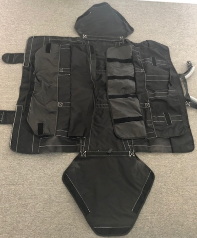 A black garment bag with multiple pockets and compartments, laid flat on a gray surface.