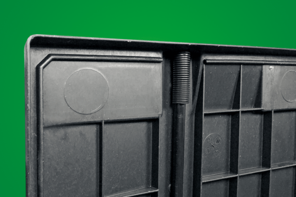 A close-up of the edge of a black plastic container, featuring a circular indentation and a textured, coiled section against a green background.