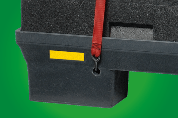 Close-up of a black plastic container with a yellow label and a securing strap, set against a green background.