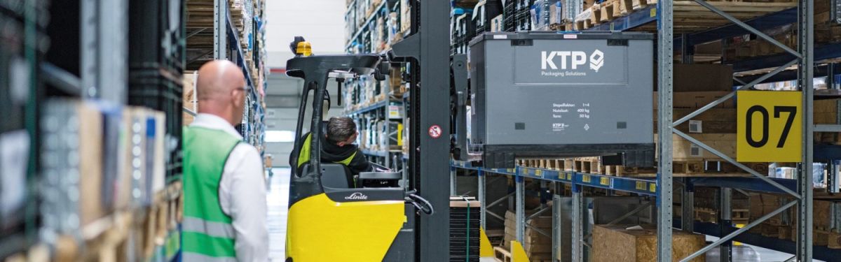 A warehouse scene showing a forklift operator handling packaging solutions containers, with shelves filled with various goods and a visible aisle sign labeled "07".