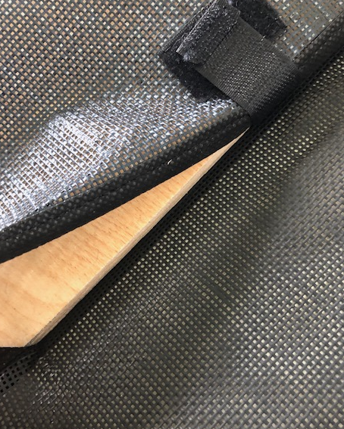 Close-up of a textured black material partially covering a light wooden surface, secured with a strap.