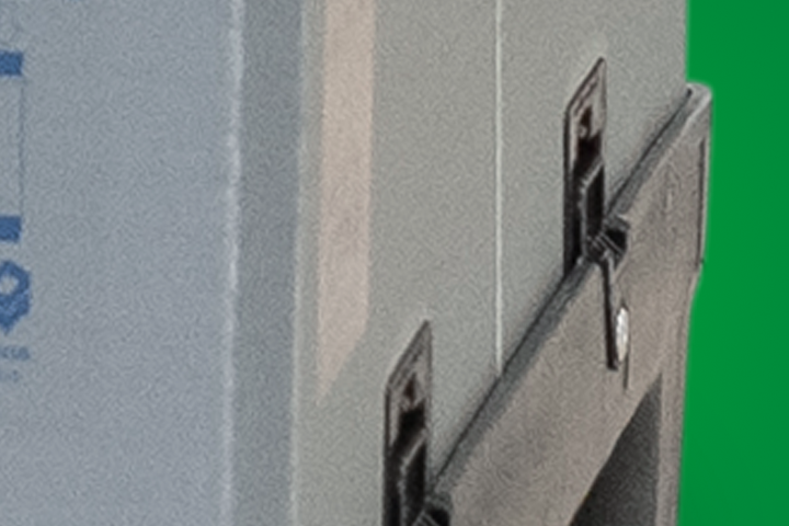 An industrial plastic container with a grey side and black base, partially visible against a green background.