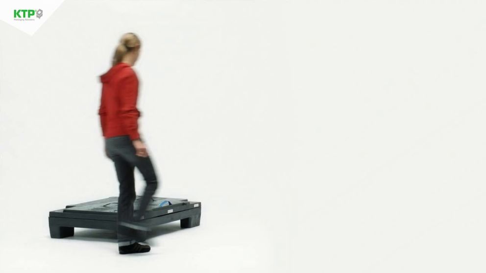 A person in a red hoodie walking past a large flat object on a white background.