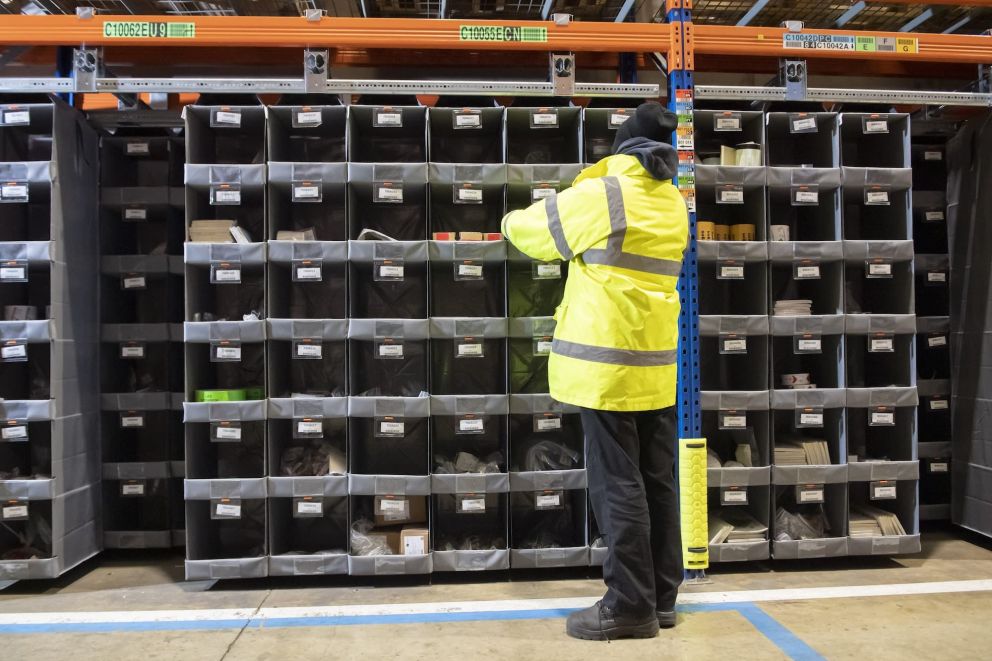 A person in a yellow coat that is picking orders in a Storeganizer rack