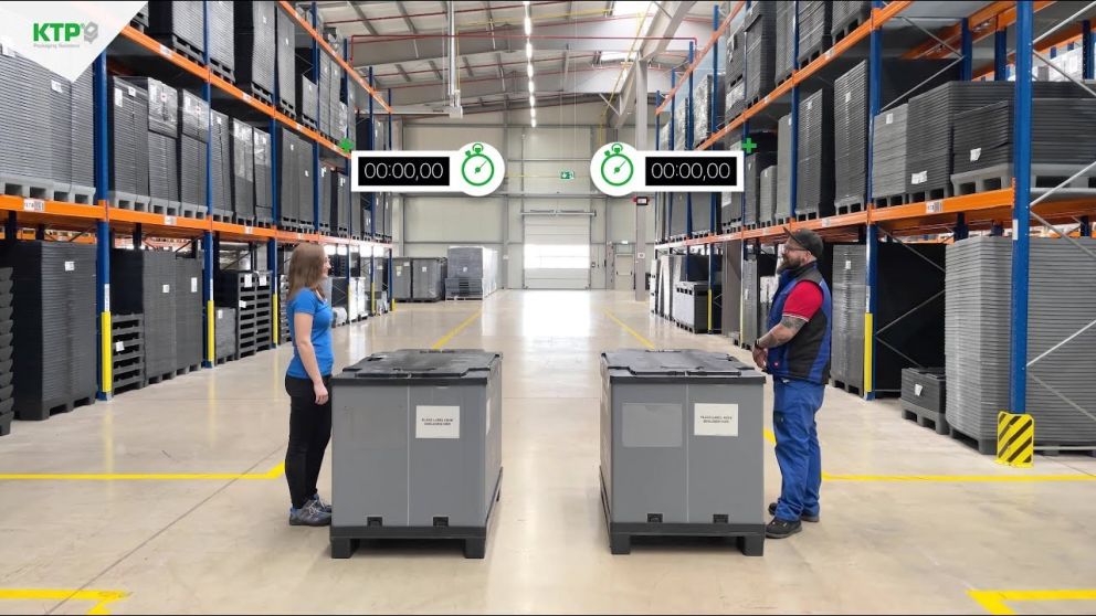 A warehouse setting with two people standing in front of gray storage containers, timers displayed above them, and shelves filled with similar containers in the background.