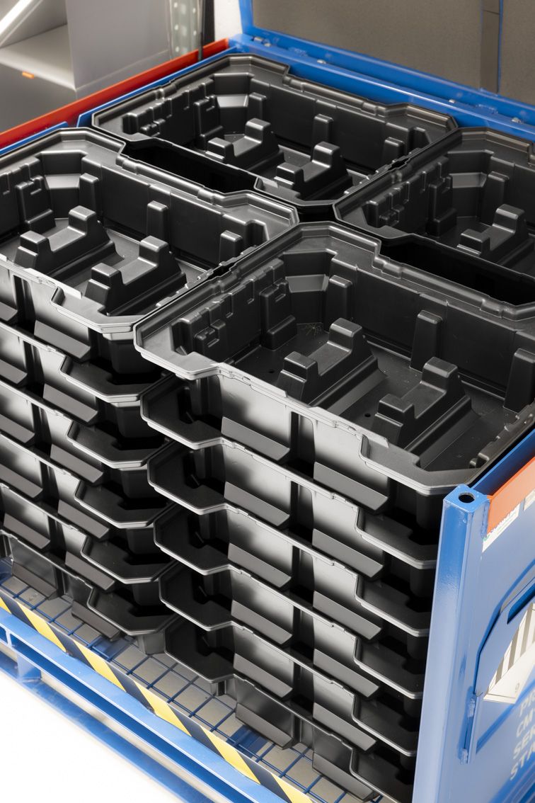 Black thermoformed trays in plastic, stacked inside of a steel rack