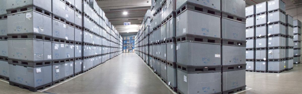A wide aisle in a warehouse lined with tall stacks of gray storage containers.