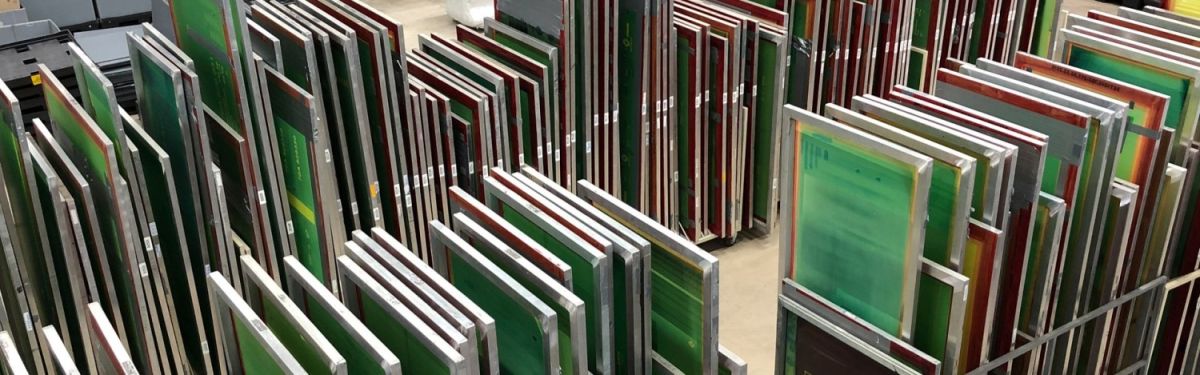 A collection of screen printing frames in various colors, organized and stacked upright in a workshop or studio setting.