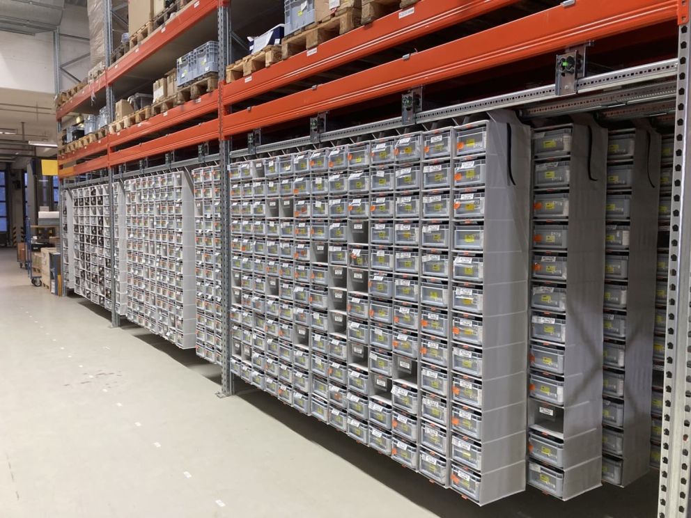 A large storage area with racks filled with labeled plastic bins and boxes.