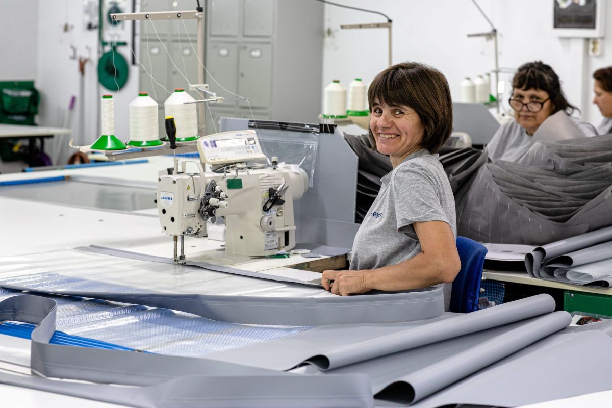 A woman working for conTeyor smiling while cutting and stitching textile