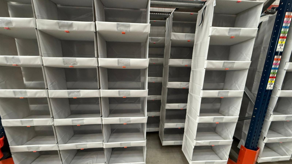 Empty shelving units in a storage area, with gray fabric and orange tags.