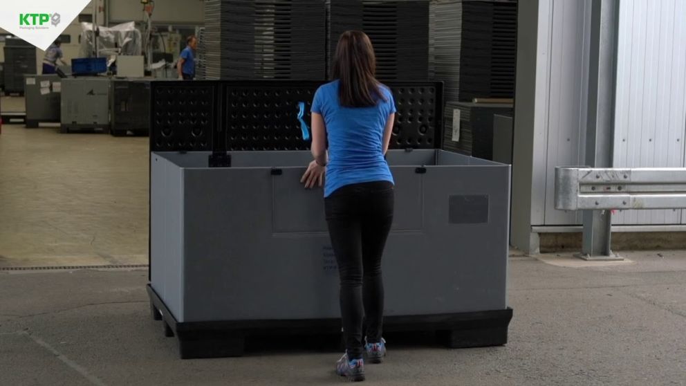 A person in a blue shirt is leaning over a large gray container in an industrial setting, with shelves and additional containers visible in the background.