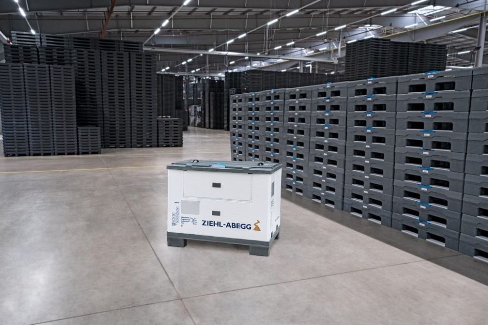 A warehouse interior featuring stacked plastic pallets in the background and a white storage unit branded with "ZIEHL-ABEGG" in the foreground.
