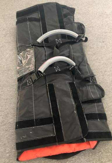 A black padded bag with orange interior, featuring two handles and Velcro straps, lying flat on a gray surface.