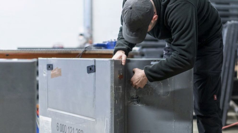 A person assembling a metal box or crate in a workshop environment.