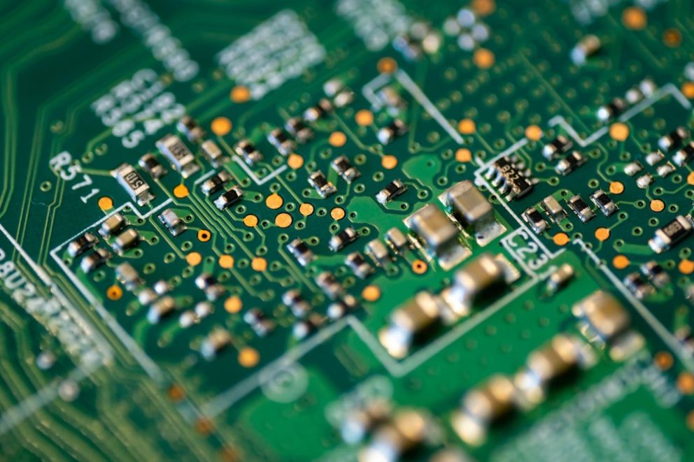 Close-up of a green printed circuit board (PCB) with various electronic components, including resistors and capacitors, and intricate silver traces connecting them.