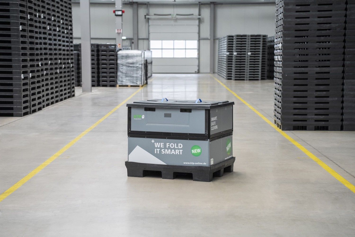 A folding storage container with text "WE FOLD IT SMART" in a warehouse setting, with stacks of pallets in the background.