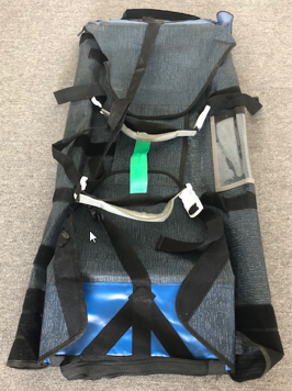 A rolled-up canvas bag with straps, featuring a blue section at the bottom and a clear pocket on the side.