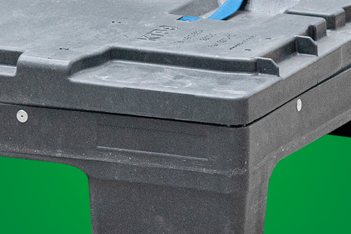 Close-up of a dark plastic storage container with a blue strap, set against a green background.
