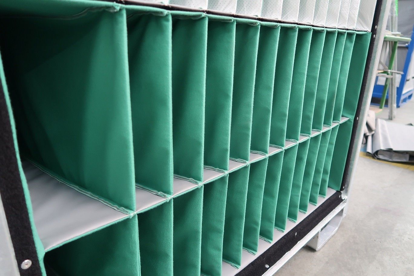 A close-up of a storage unit with multiple green fabric compartments, set against a blurred industrial background.