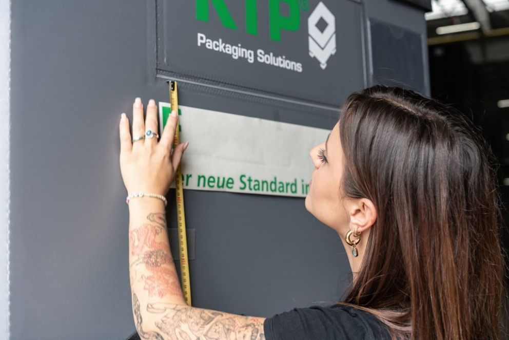 A person measuring height on a wall next to a company sign, with a focus on their hand and tattoos.