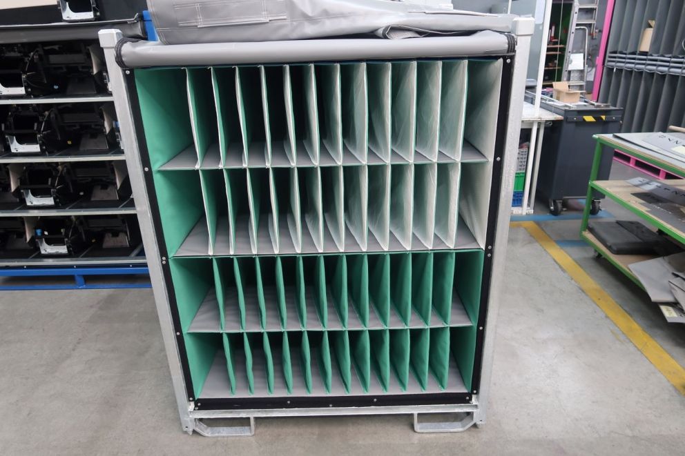 A tall, metallic storage unit with multiple compartments, lined with a green material, used for organizing items in a workspace.