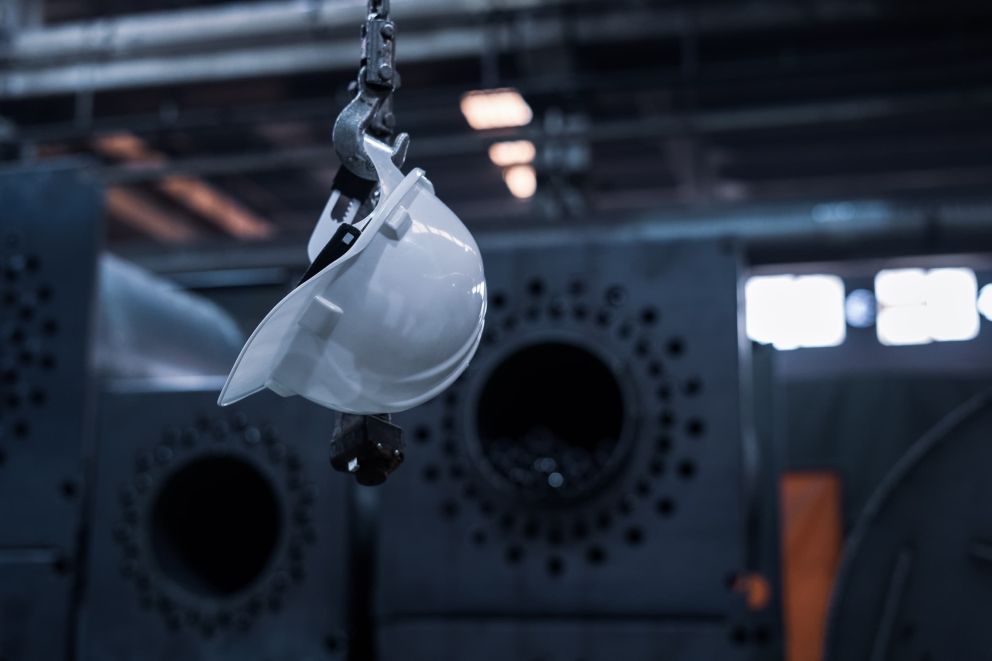 A hardhat hanging on a hook with an industrial background