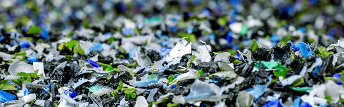 Close-up of mixed plastic fragments in various colors, including black, green, blue, and white, scattered throughout the image.