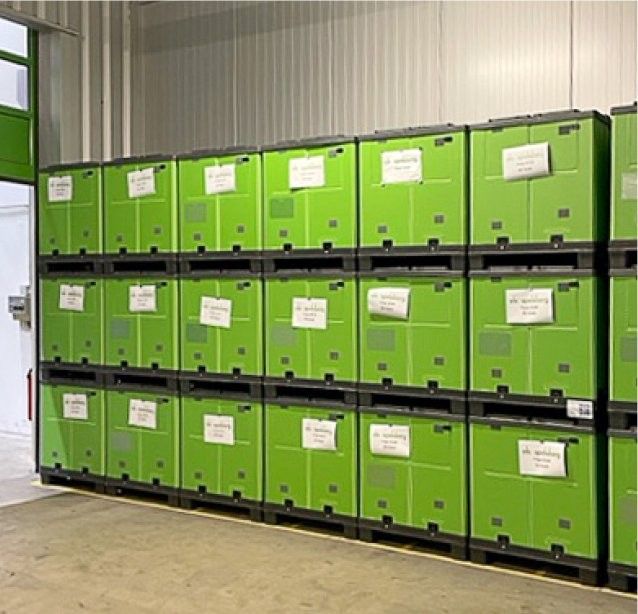 A wall of green storage bins stacked in rows, each labeled with a white tag, inside a storage facility.