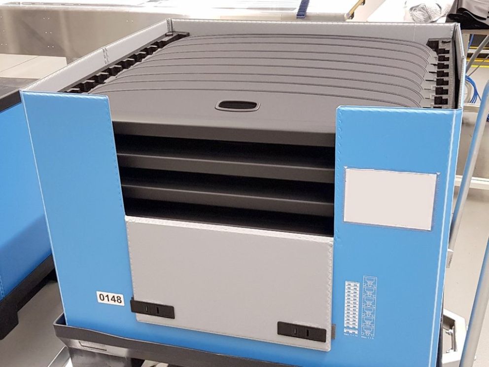 A stackable container with black removable trays, featuring blue and gray sides and a small identification label on the front.