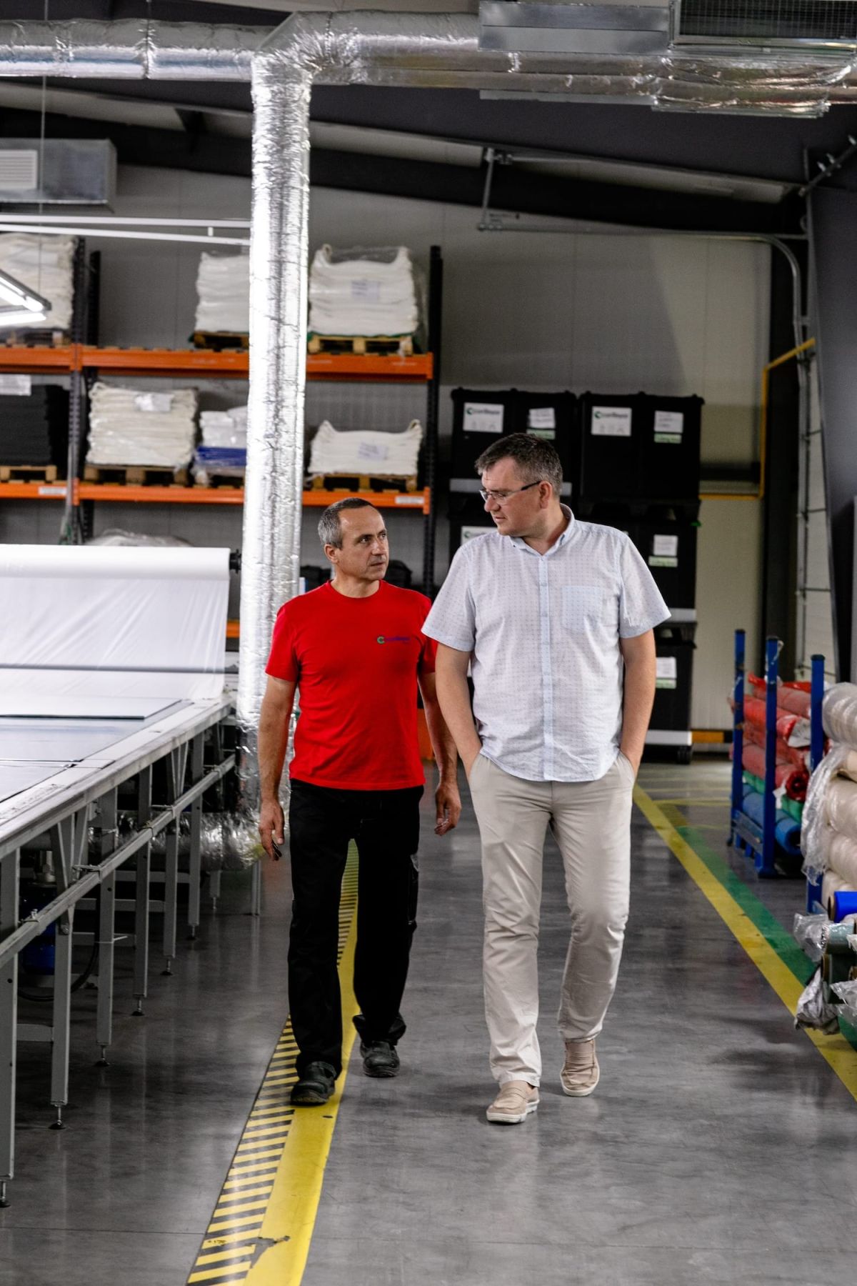 Two men walking towards the camera. They're in a factory talking to eachother.