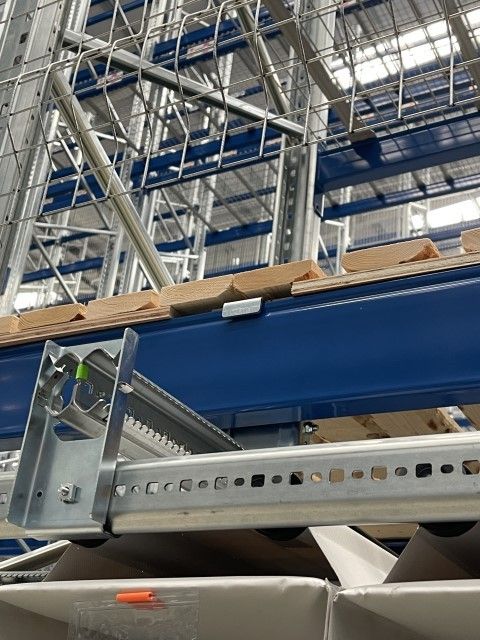 Close-up view of a metal shelving unit with wooden pallets stacked above, featuring structural supports and storage components in a warehouse setting.