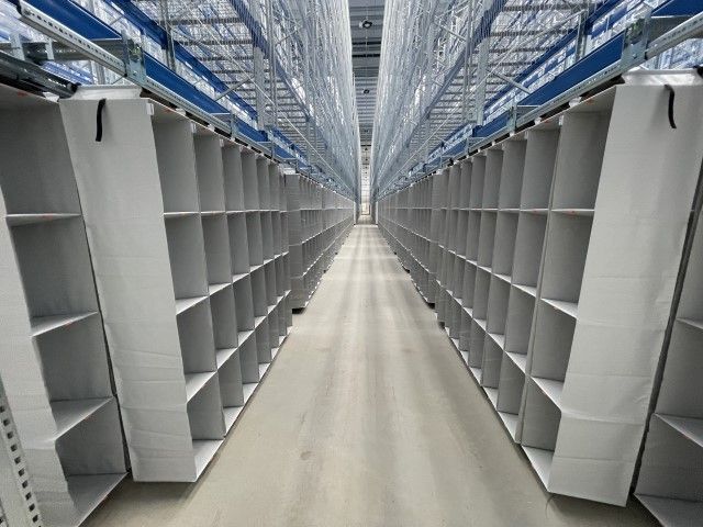 A narrow aisle between tall shelving units in a warehouse, with empty shelves on both sides.