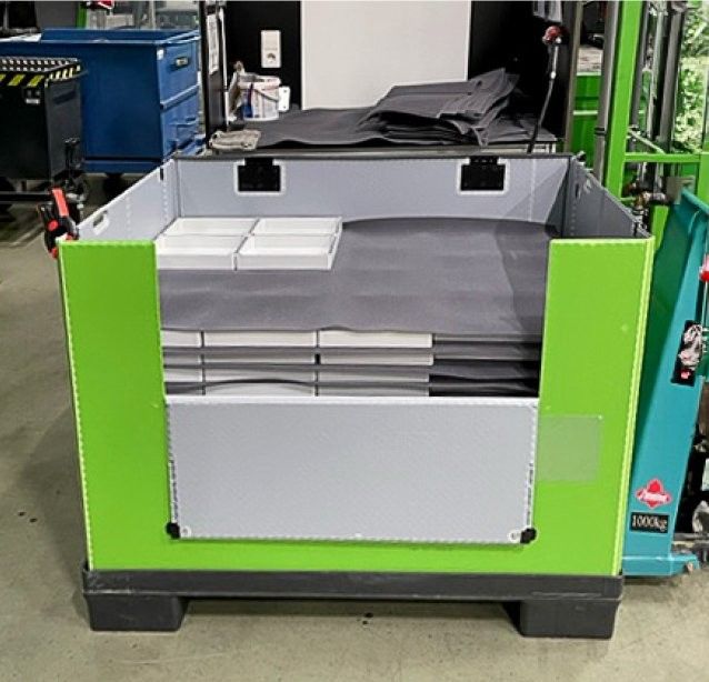 A green and gray storage container filled with stacked gray materials and several white boxes, situated in a warehouse environment.
