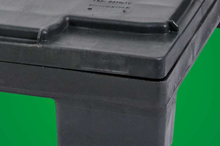 Close-up of a black plastic pallet with a smooth surface and edges, set against a green background.